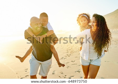 Cheerful black man and woman walking and carrying their children in evening sandy shore.