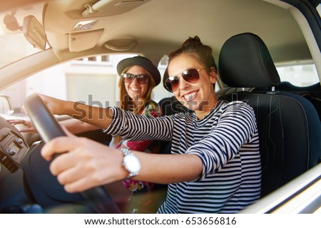 Two attractive friendly young women enjoying a day trip to town viewed through the open window of their car grinning happily at the camera