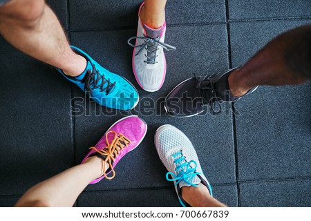 High angle of a group of people\'s feet wearing running shoes standing together in a huddle on a gym floor