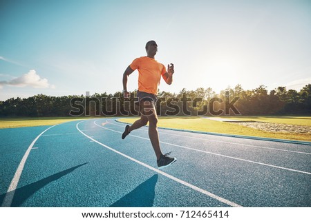 Fit and focused young African male athlete running alone along a race track while out training on a sunny day