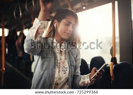 Young woman smiling while riding on a bus listening to music on a smartphone