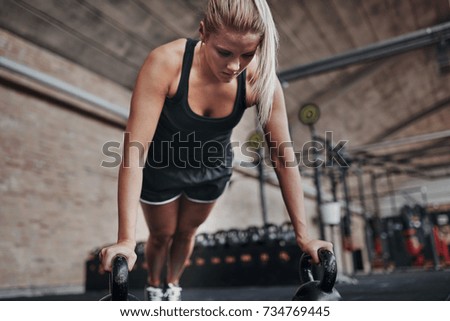 Focused young blonde woman in exercise clothing working out alone with weights on a gym floor