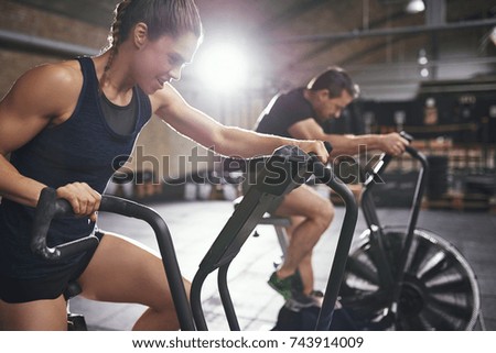 Young male and female wearing sportswear riding toughly cycling machines in light modern gym.