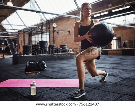 Fit young blonde woman in exercise clothing doing core exercises with a swiss ball while working out alone in a gym