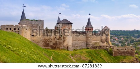 The panorama of old fortress with ramparts and towers. The high stone walls. In the foreground is green hill, below of the fortress on the background - the city. Sunny day. Ukraine.