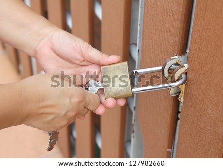 Closeup image of hand use key to open padlock and the brown wooden door