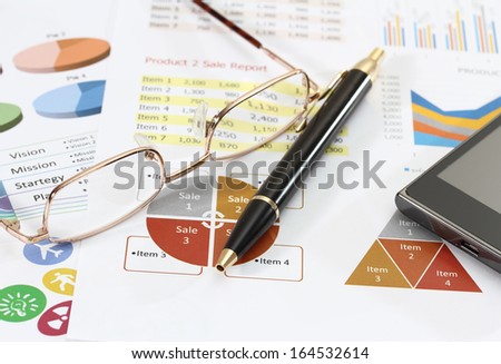 closeup image of graphics and finance report for business with pen mobile phone and coffee