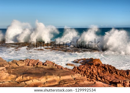 Row of wave splashes on red rock beach. Shot in the Cape of Good Hope and Cape Point Nature Reserve, Table Mountain National Park, near Cape Town, South Africa.
