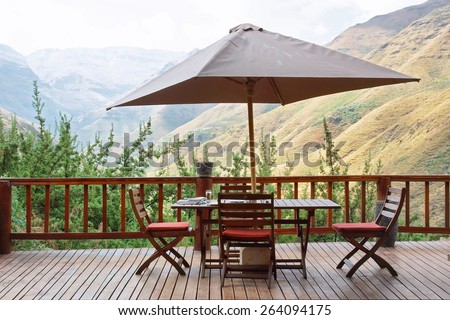 Table and chairs under umbrella on terrace against awesome mountains. Shot in Tsehlanyane Nature Reserve, Lesotho.