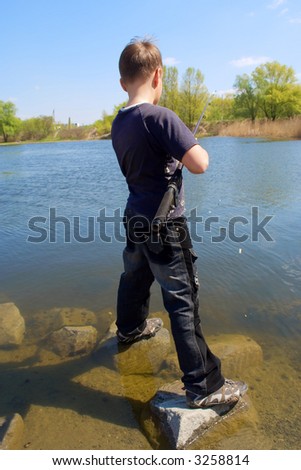 Fishing boy stands on underwater stones. Shot near the Dnieper river, Ukraine.