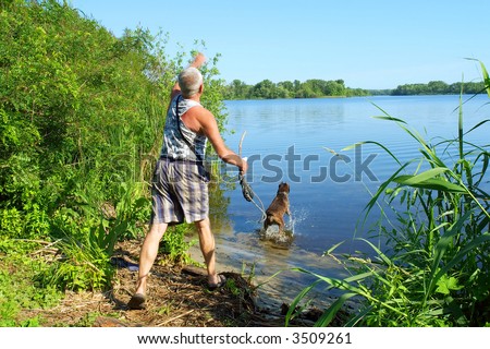 Old man plays with his dog on river shore - throws a stick (man has motion blur). Shot in June near Dnieper river, Ukraine.