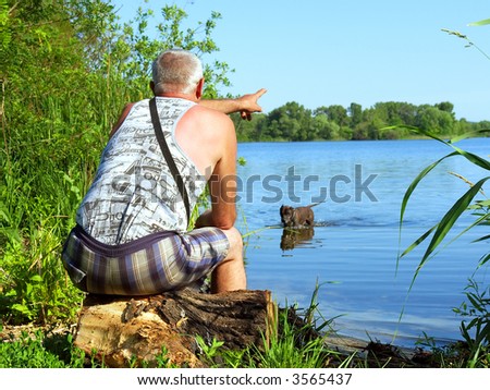 Old man directs his dog where to look after stick - in sunrise light (focus on man). Shot in June near Dnieper river, Ukraine.