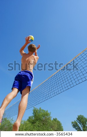 Teen playing beach volleyball - jumps high to serve the ball. Shot near Dnieper river, Ukraine.