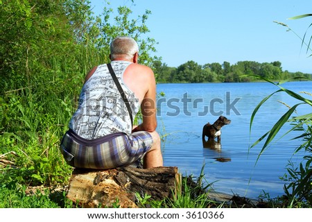 Grey-haired oldman sits on river shore and looks at his fight dog. Shot in June near Dnieper river, Ukraine.
