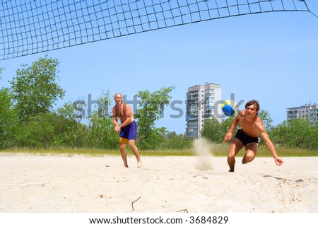 Two men playing beach volleyball - teenager falls on sand to catch ball. Shot near Dnieper river, Ukraine.
