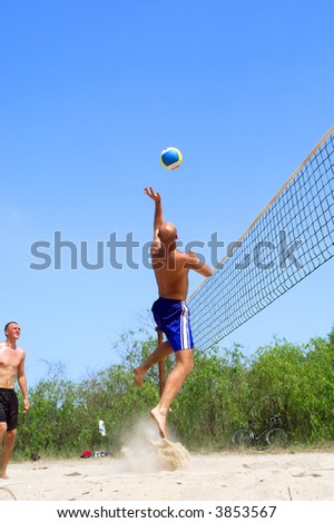 Two men playing beach volleyball - balding man jumps high to catch ball. Shot near Dnieper river, Ukraine.
