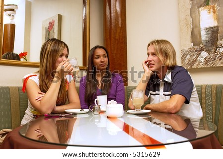 Two mulatto girls are listening to blond guy while drinking coffee in a cafe. Shot in Western Cape, South Africa.