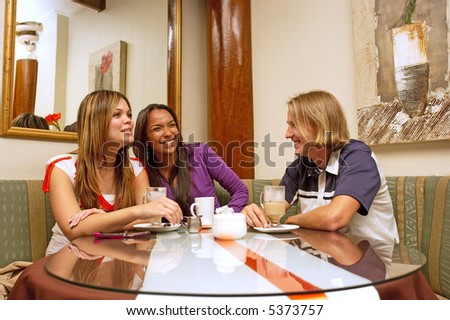 Two mulatto girls and blond man drink coffee and laugh in a restaurant. Shot in Western Cape, South Africa.