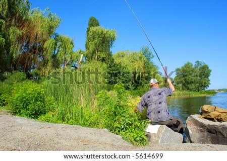 Sitting fisherman casts the rod  into morning river. Shot in June near Dnieper river, Ukraine.