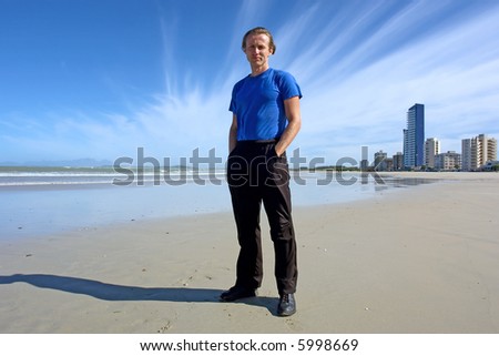 Man stands on beach with majestic sky and sky-scrapers. Shot in Strand, Western Cape, South Africa.