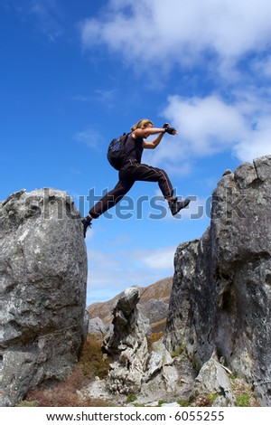 Man with long hair jumps from rock - low angle, against sky. Shot in Hottentots-Holland Mountains nature reserve, near Grabouw, Western Cape, South Africa.