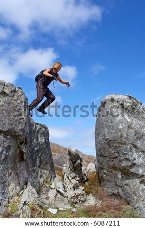 Young man jumps from rock with smile - low angle, against sky. Shot in Hottentots-Holland Mountains nature reserve, near Grabouw, Western Cape, South Africa.