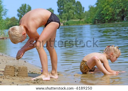 Kids play on beach in hot summer day - girl sits in water, boy makes sand castle. Shot in July, Dniepropetrovsk, Ukraine.