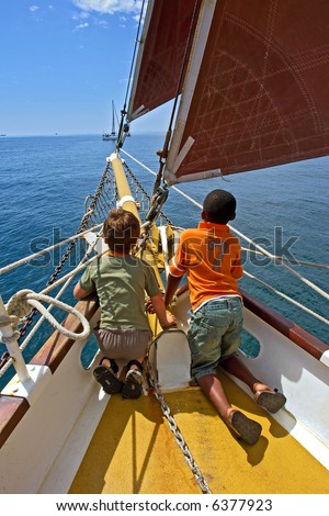 Two boys, black and white, play on yacht\'s deck. Shot during yacht cruise in Waterfront, Cape Town, South Africa.