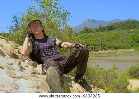 Happy hiker talks over phone while lying on rocks - and mountains are background. Shot in Stellenbosch Mountain, Western Cape, South Africa.