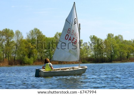 Brave child alone navigates small yacht through spring river. Shot in Ukraine.