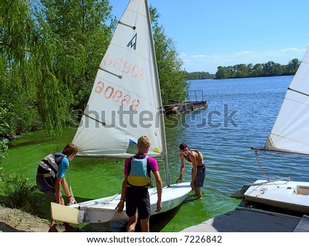 Three teens launch a yacht on river. Shot in July, Dnieper river, Ukraine.