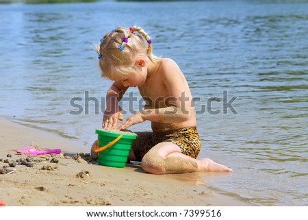 Little blond girl plays on beach with toy bucket in hot summer day. Shot in Ukraine.