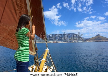 Timid girl on yacht with red sails looks at waves and Table Mountain as a background. Shot during yacht cruise in Waterfront, Cape Town, South Africa.