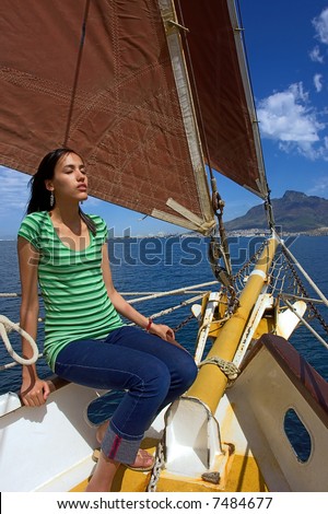 Sunbathing girl on yacht with red sails and Table Mountain as a background. Shot during yacht cruise in Waterfront, Cape Town, South Africa.