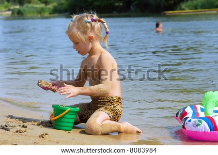 Dirty girl plays with sand on beach in hot summer day. Shot in July, Ukraine.