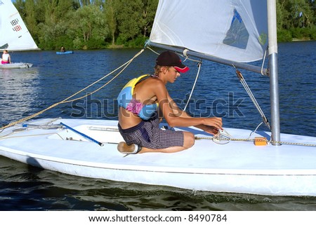 Teen boy adjusts yacht\'s gear on river. Shot in July, Dnieper river, Ukraine.