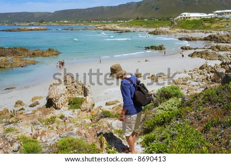 Woman walks down to beach among awesome mountains. Shot on Cliff Path near Hermanus, Walker Bay, Western Cape, South Africa.