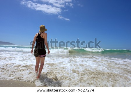 Woman on sea beach enters the water. Shot in Hermanus, Walker Bay, Western Cape, South Africa.