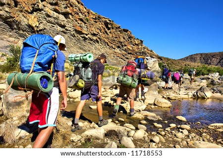 Group of hikers crosses small river in mountains. Shot in the Langeberge highlands near Grootrivier and Gouritsrivier rivers crossing, Garden Route, Western Cape, South Africa.