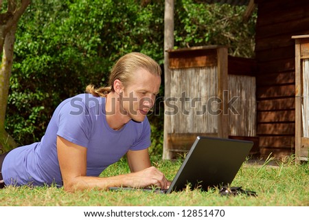 Young man with laptop on grass next to rural house - closeup. Shot in Sodwana, KwaZulu-Natal province, South Africa.