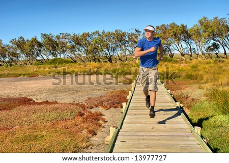 Young man jogs on woodwalk above mangrove marshland. Shot in West Coast Nature Reserve, near Langebaan, Western Cape; South Africa.