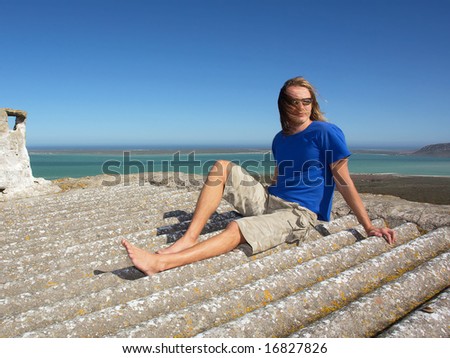 Young man with long hair on roof of house in windy day. Shot in West Coast Nature Reserve, near Langebaan, Western Cape; South Africa.