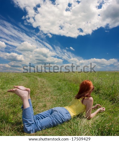 Red-hair girl lying barefoot in field with wild flowers. Shot in Ukraine.