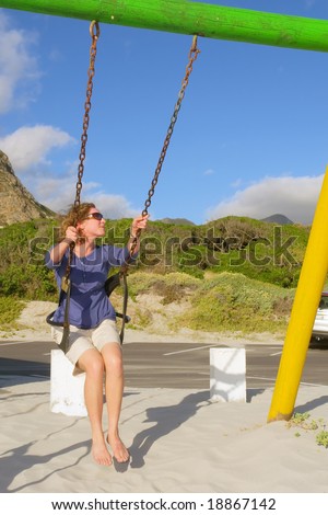 Happy woman on swings on beach among awesome mountains. Shot in Hermanus, Walker Bay, Western Cape, South Africa.