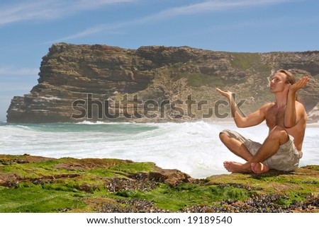 Young man prays to sun sitting on rocks - sea-misty mountain background. Shot in the Cape of Good Hope and Cape Point Nature Reserve, Table Mountain National Park, near Cape Town, South Africa.