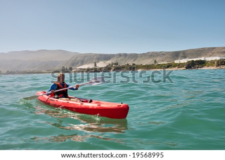 Young man in sea kayak against mountains. Shot in Hermanus during the whale watching season, Western Cape, South Africa.