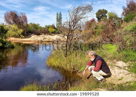 Old man sits next to river in mountains. Shot next to Olifant (Elephant) river, near Citrusdal, Western Cape, South Africa.