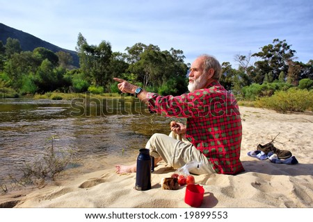 Old man points somewhere while having lunch - sitting next to river in mountains. Shot next to Olifant (Elephant) river, near Cederberg, Western Cape, South Africa.