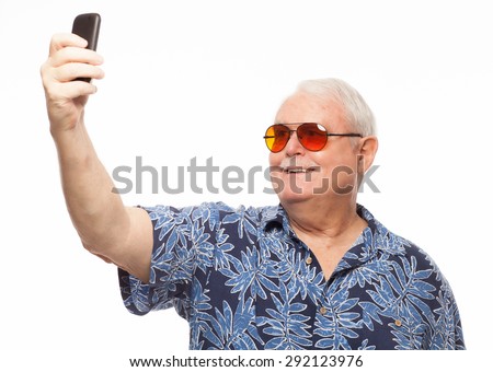 Senior man wearing loud hawaiian shirt on white background taking photo selfie with mobile phone.