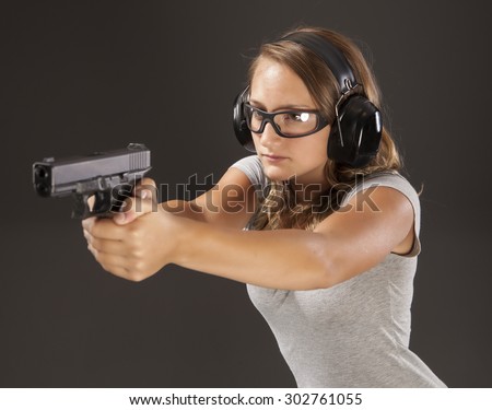 PERSONAL DEFENSE, GUN SAFETY | Young woman learning proper gun control and weapon safety, wearing proper safety glasses and ear protection.  Her finger is straight and off the trigger.